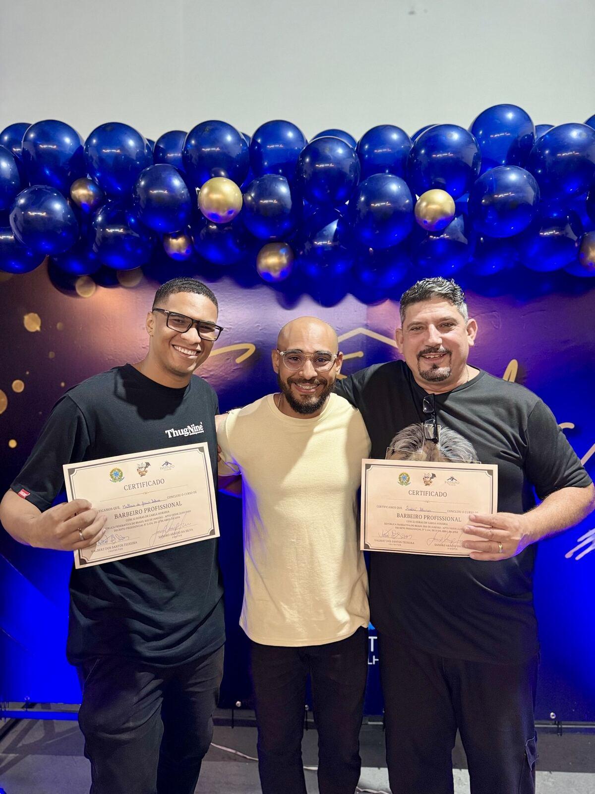 Dois formandos do curso de Barbeiro com o professor, cada um com o seu certificado